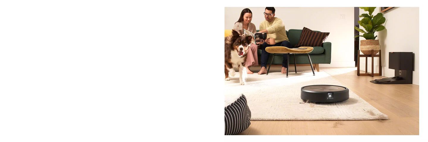l’aspirateur Roomba® aspire des poils de chien, un couple et un chien sont à l’arrière-plan